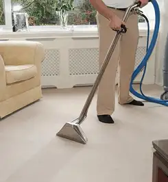 Professional carpet cleaner using a hot-water extraction wand and hose machine in a living room in Austin, TX.
