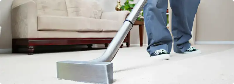 Carpet cleaning technician using a hot-water extraction wand on a light-colored carpet in a living room, Austin, TX.