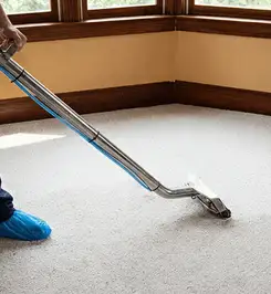 Steam carpet cleaning technician using a hot-water extraction wand on a residential carpet, wearing blue protective shoe covers Austin, TX.