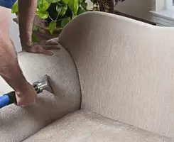 Professional upholstery cleaner deep-cleaning a fabric sofa with a handheld extraction tool and hose in Austin, TX.
